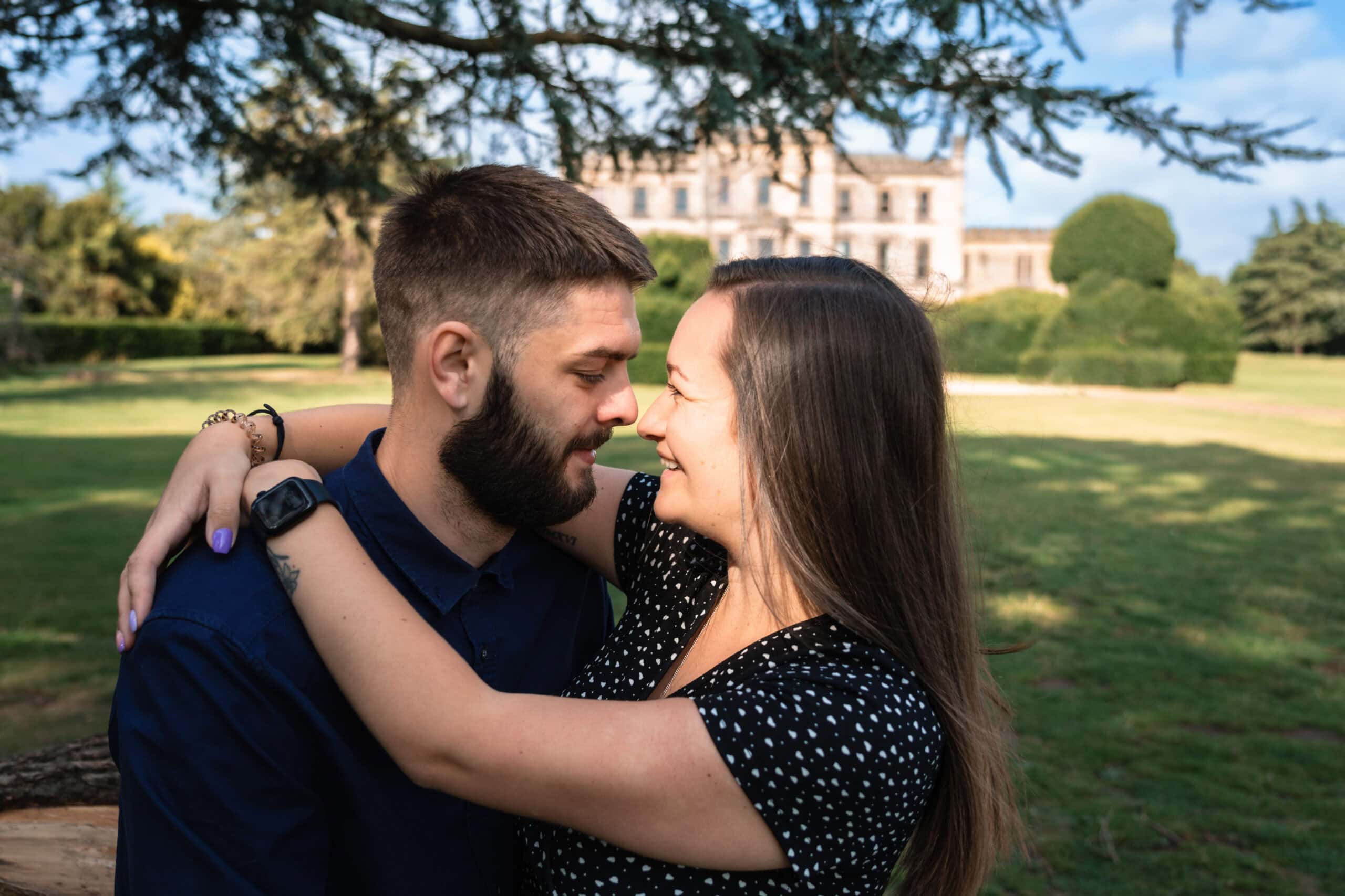 Couple embracing in a garden near historic building.
