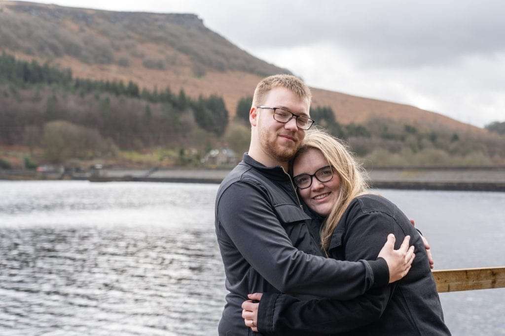 couple hugging looking at the camera with a backdrop of Ladybower Reservior