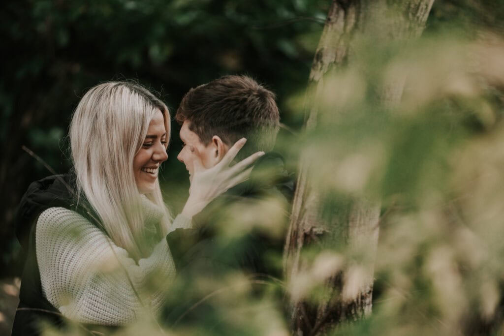 Couple smiling in a forest setting.