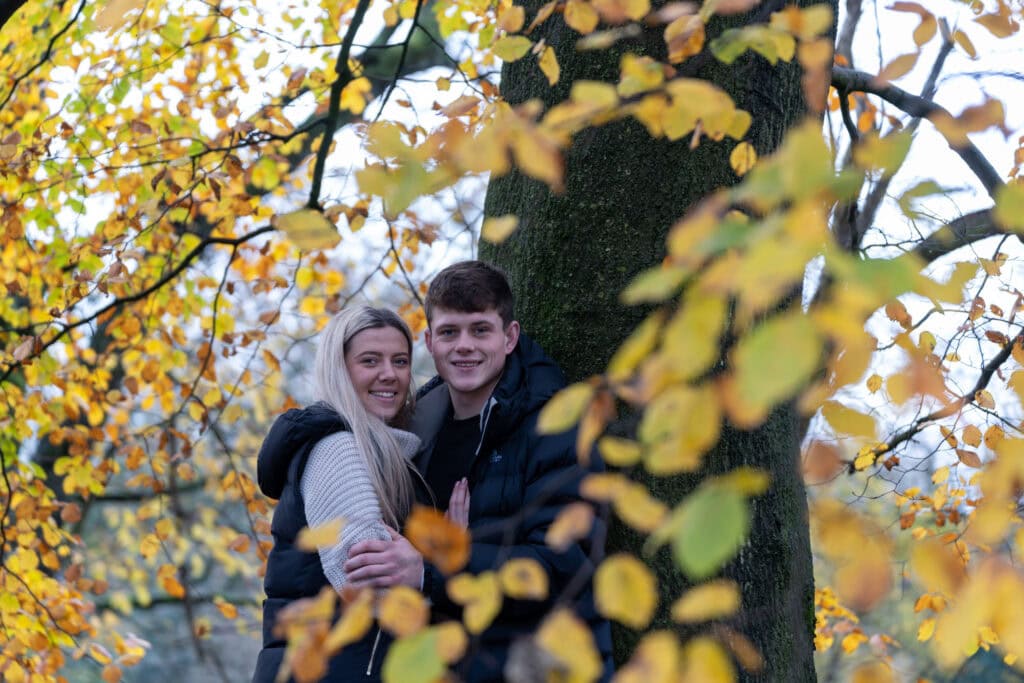 Couple smiling under autumn leaves by tree