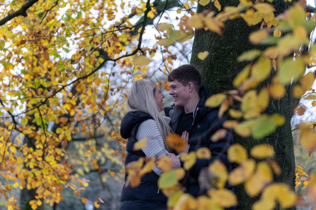 Couple smiling near tree with autumn leaves.