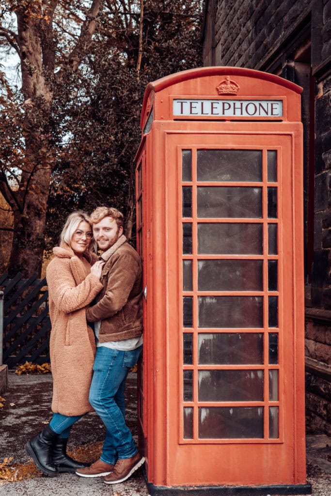 Couple hugging beside red phone booth outdoors.