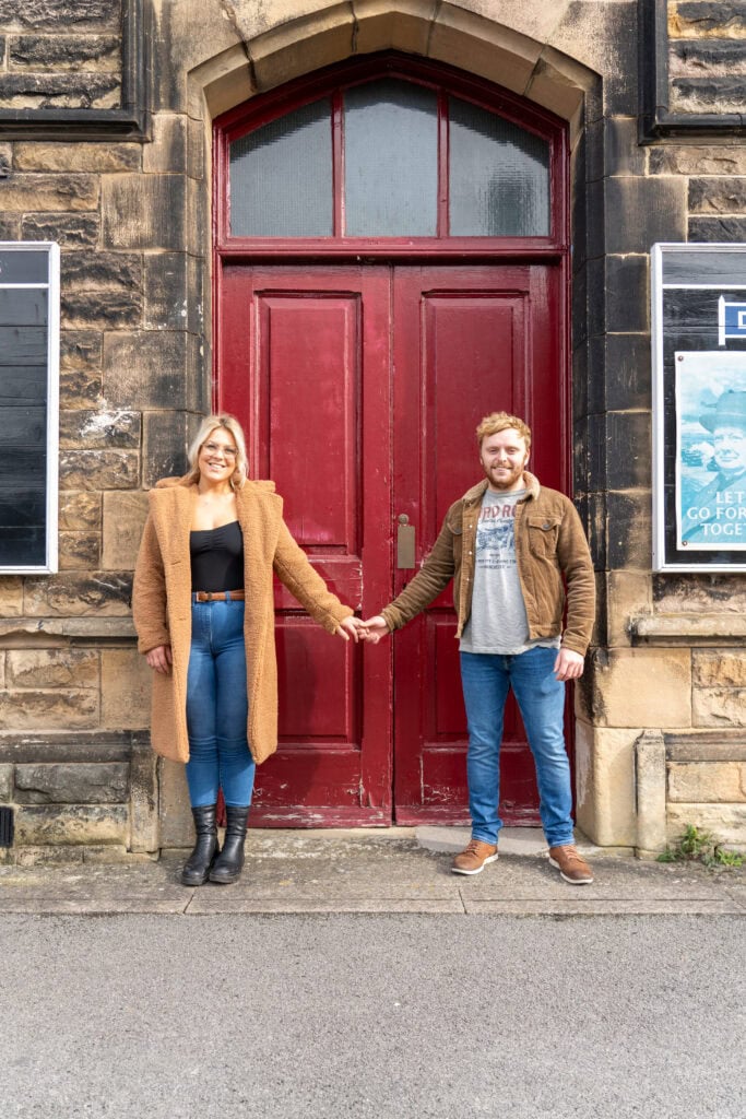 Couple holding hands in front of red door.