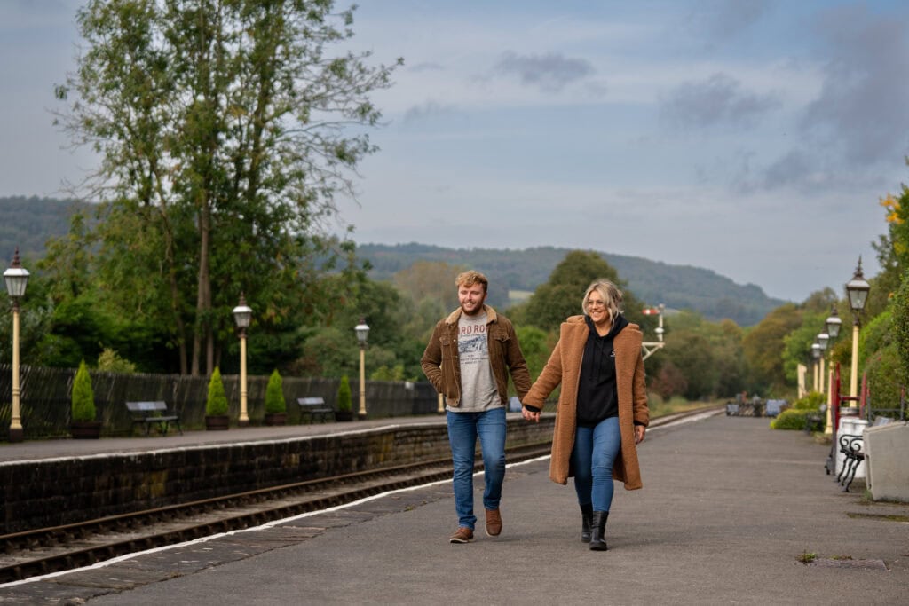 Couple walking on train platform, countryside background.