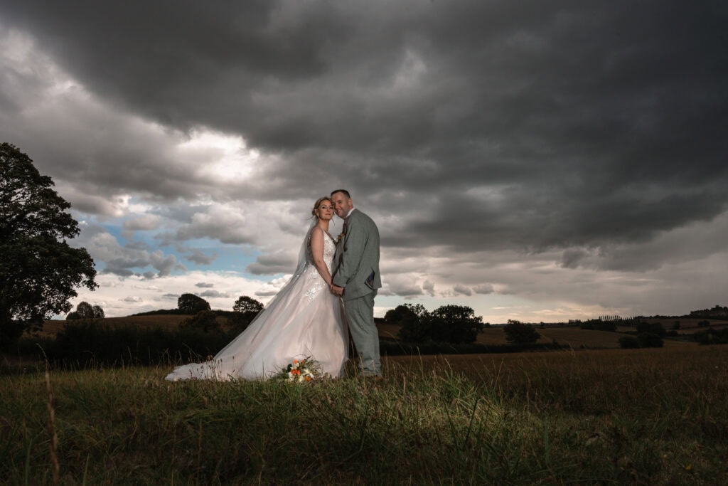 Bride and groom in cloudy countryside wedding portrait.